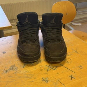 Jordan 4s black cats - Säljer ett par svarta Nike Air Jordans med snörning och ikonisk design. Skorna har ingen box 
