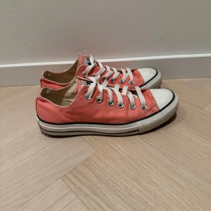 Orange sneakers från Converse - Säljer ett par klassiska orange Converse All Star sneakers med vita snören och tåhätta. Skorna har en låg profil och den ikoniska loggan på hälen. Perfekta för en avslappnad stil.