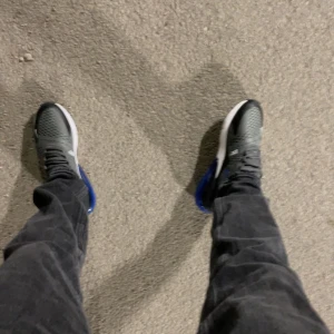 Nike Air Max 270 i grå och blå - Säljer ett par Nike Air Max 270 sneakers i grått och blått. De har en snygg design med en stor synlig Air-enhet i hälen för extra komfort. Perfekta för både vardag och träning. Skorna har snörning och är i mycket bra skick.