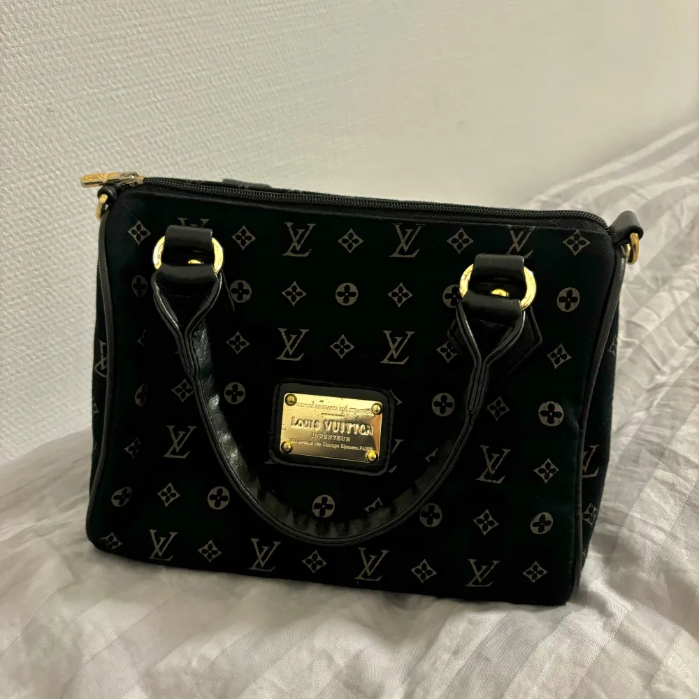 Säljer en elegant svart handväska från Louis Vuitton med det klassiska monogrammönstret. Väskan har guldfärgade detaljer och en praktisk dragkedja. Perfekt för både vardag och fest! Den är i bra skick förutom lite i innerfodret (bild 5). Köpt här på plick för några månader sedan och säljaren garanterade äktheten. . Väskor.