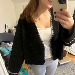 Svart croppad jacka med vita detaljer - Säljer en svart croppad jacka med vita sömmar. Den har en loose passform och långa ärmar. Perfekt för höst och vår, och funkar både till vardags och fest. Superfin att matcha med jeans eller kjol!