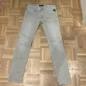 Grå jeansbyxor från Replay - Snygga grå jeansbyxor från Replay, modell Anbass. De har en klassisk femficksdesign och en rak passform. Perfekta för en stilren look. storleken på jeansen är 33 i midjan och 34 på längden. Säljes för att dem aldrig kommer till användning. Köpte dem för 1200 kr.