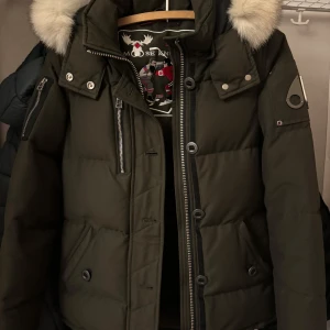 Olivgrön dunjacka från Moose Knuckles - Säljer en olivgrön dunjacka från Moose Knuckles i mycket bra skick. Jackan har en fluffig pälsfodrad huva och snygga detaljer med dragkedjor och knappar. Perfekt för kalla vinterdagar! Den är köpt på NK 2022 använd fåtal gånger tyvärr passar den inte mig längre men den är superfin och i mycket bra skick! ❄️ den är i stl XS men passar även XXS normal i storleken. 