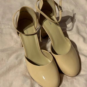 Beige pumps med rem - Säljer ett par eleganta beige pumps med en smal rem runt ankeln. Skorna har en rund tå och en bekväm klack som passar perfekt för både vardag och fest. De är i nyskick och redo att användas för att komplettera din outfit.