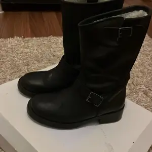 Säljer ett par svarta boots från Ella of Sweden i storlek 39. De är gjorda i skinn och har en snygg spänndetalj på sidan. Insidan är fodrad med mjukt material för extra värme och komfort.  Använt bara ett par gånger. Perfekta för höst och vinter! 