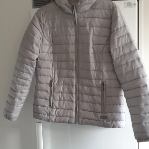 Grå pufferjacka från Champion - Snygg och bekväm pufferjacka från Champion. Jackan har en dragkedja framtill och två praktiska fickor med dragkedjor. Perfekt vardagsjacka. Färgen är grå/silver, men går lite åt det blå/gröna hållet. Är som en storlek 38/40. Nypris 1200kr