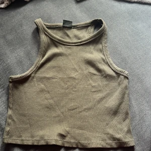 Olivgrön ribbad linnetopp från Gina Tricot - Säljer en snygg olivgrön ribbad linnetopp från Gina Tricot. Toppen är ärmlös och har en tight passform, perfekt för sommardagar eller som ett lager under en jacka. Den är i storlek M och i bra skick.