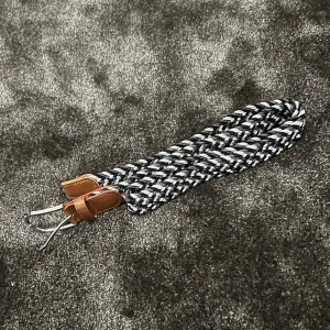 Flätat bälte med bruna detaljer - Säljer ett snyggt flätat bälte i svart och vitt med bruna läderdetaljer. Bältet har en cool, modern look och passar perfekt till både vardag och fest. Spännet är i silverfärgad metall och ger en stilren touch. Perfekt för att ge din outfit det där lilla extra!
