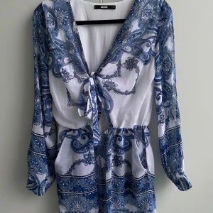 Blå jumpsuit - Blå/vit jumpsuit med shorts och långa ärmar. Stretchiga i midjan och öppna ärmar, knytning fram, passar lång överkropp