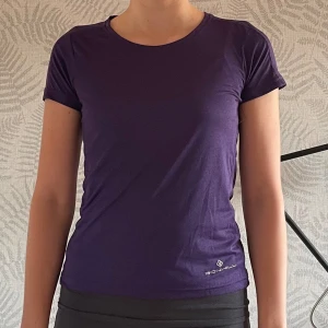 Lila t-shirt från Ronhill - Säljer en snygg lila t-shirt från Ronhill i storlek XS. Den är gjord av 100% polyester vilket gör den perfekt för träning. T-shirten har en tight passform och korta ärmar, vilket gör den både bekväm och stilren. Perfekt för dig som vill ha något enkelt men funktionellt!
