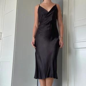 Svart siden klänning - Så fin svart siden klänning! Fin detalj på ena sidan och en slit på vänster sida, längden är under knäerna. Passar perfekt till en fest eller middag! Det står ingen storlek, men det passar bra på mig som bär M/storlek 38. Inga defekter! ❤️‍🔥