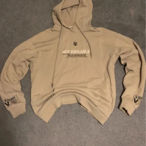 Beige Hoodie Med Roligt Tryck  - Beige hoodie med rolig quote som tryck ”NOT AVAILABLE : Sorry, the vagina you are trying to reach is no longer available”. Står både på rygg och på ärmar. Sitter bra och är mysig. Inga tecken på slitage förutom ett ytterst litet hål i ryggen. 