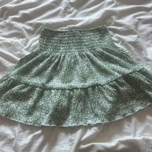 Grön blommig kjol - Säljer en superfin grön blommig kjol med volangdetaljer. Den har en elastisk midja som gör den bekväm och lätt att bära. Perfekt för sommardagar eller en avslappnad vårutflykt. Kjolen är i bra skick och redo för nya äventyr! 🌸