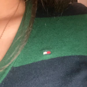 Randig tröja från Tommy Hilfiger - Säljer en snygg och bekväm randig tröja från Tommy Hilfiger. Den är grön och svart med långa ärmar och en liten logga på bröstet. Perfekt för både vardag och lite finare tillfällen!