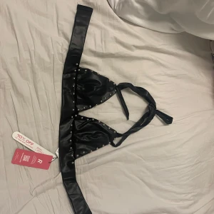 Svart satin korsett från Romwe - Snygg svart satin korsett från Romwe med nitar och knytband i ryggen. Perfekt för en edgy look. Helt ny med tag kvar.