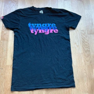 Svart t-shirt från Tyngre - Snygg svart t-shirt från Tyngre med färgglatt tryck i blått, lila och rosa. Perfekt för en avslappnad stil. Tillverkad i mjukt material för extra komfort. Använd ett få antal gånger men tvättlappen är borta 🖤 köpt på herravdelningen 