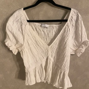 Vit blus från Bershka - Säljer en söt vit blus från Bershka med korta puffärmar och volangdetaljer. Blusen har en v-ringad design och är tillverkad i ett lätt och luftigt material, perfekt för varmare dagar.🌞☺️