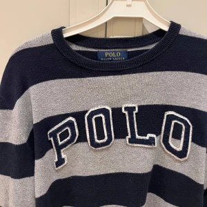 Randig tröja från Ralph Lauren - Snygg randig tröja från Ralph Lauren i marinblått och grått. Tröjan har långa ärmar och ett stort 'POLO' tryck på framsidan. 