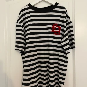 Randig t-shirt från H&M - Säljer en svartvit randig t-shirt från H&M med ett rött LA-tryck. T-shirten har korta ärmar och en rund halsringning. Perfekt för en avslappnad stil. Alla priser kan diskuteras!