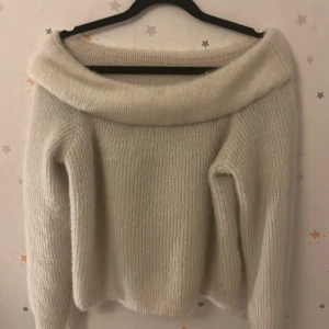 Vit stickad offshoulder-tröja från DIVIDED - Säljer en mysig vit stickad offshoulder-tröja från DIVIDED. Perfekt för kyliga dagar med sin mjuka och bekväma passform. Tröjan har långa ärmar och en bred krage som ger en stilren look.