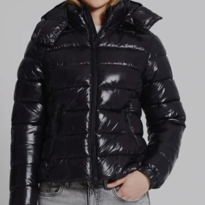 Lager157, Nikki jacka svart  - Snygg svart pufferjacka med glansig yta och dragkedja framtill. Jackan har en hög krage och långa ärmar, perfekt för kyliga dagar. Den quiltade designen ger extra värme och stil.
