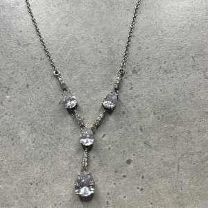 Silverfärgat halsband med glittriga stenar - Elegant silverfärgat halsband med flera glittriga stenar i en vacker droppformad design. Perfekt för att ge en touch av glamour till din outfit.