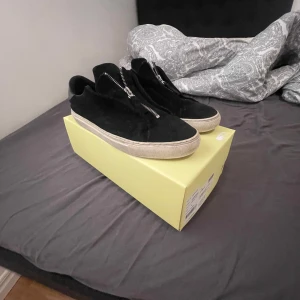  Axel arigato skor med dragkedja - Snygga svarta sneakers med dragkedja framtill och en tjock vit sula. Perfekta för en stilren look med en twist. Skorna har en modern design och är lätta att matcha med olika outfits.