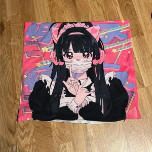 Kawaii kuddfodral med anime-motiv - Färgglatt kuddfodral med ett anime-motiv i rosa och lila toner. Designen visar en karaktär med stora ögon och rosa detaljer som hörlurar och rosett. Perfekt för att ge ditt rum en söt och unik touch. I bra skick🌸🤍. Skriv om frågor!