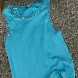 Turkos ärmlös topp med spetsdetaljer - Snygg turkos ärmlös topp från Bik Bok med vackra spetsdetaljer längs halsringningen och ärmhålen. Perfekt för varma dagar eller som ett lager under en kofta.❤️kan skicka fler bilder🫶