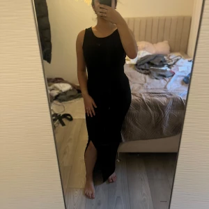 Svart ärmlös klänning - Snygg svart ärmlös klänning med en slits på sidan. Perfekt för en elegant och stilren look. Klänningen har en tight passform som framhäver figuren.