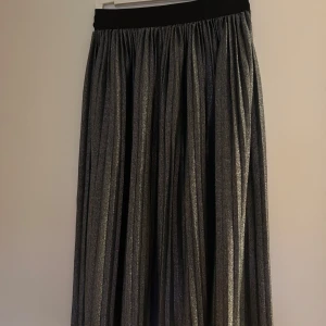 Glittrig långkjol med resårmidja - Snygg och elegant långkjol i glittrigt material med en bekväm resårmidja. Perfekt för att lysa upp vilken outfit som helst. Kjolen har ett vackert fall och är lätt att matcha med olika toppar.