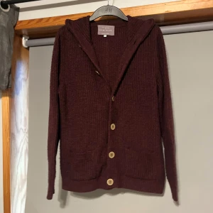 Vinröd stickad cardigan jacka - Mysig vinröd stickad kofta med huva och knappar framtill. Perfekt för kyliga dagar med sin långa ärm och bekväma passform. Ett måste i garderoben för höst och vinter!