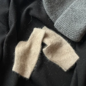 Beige stickade handskar - Säljer ett par mjuka och varma beige stickade handskar. Perfekta för kyliga dagar med en stilren design och ribbstickade muddar. De är fingerlösa vilket ger extra rörelsefrihet. Passar bra till både vardag och mer avslappnade tillfällen.