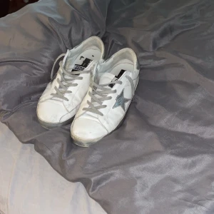 Vita sneakers med stjärndetalj - Snygga vita sneakers med en grå stjärna på sidan och grå snörning. Perfekta för en avslappnad stil.golden goose strl 42! Skriv för mer och bättre bilder! 