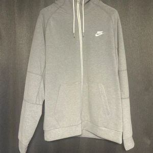 Grå hoodie från Nike - Säljer en stilren grå hoodie från Nike med dragkedja och justerbar huva. Perfekt för en avslappnad look. Den har praktiska fickor framtill och en diskret Nike-logga på bröstet. Den är oanvänd. Köpt för 699kr!! Pris kan diskuteras!! För mer bilder/videos skriv!!