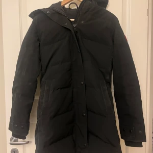 Shelburne parka Canada Goose - Säljer en svart Shelburne Parka från Canada Goose med pälsdetalj på huvan. Jackan har en långärmad design och stängs med dragkedja och knappar. Perfekt för kalla vinterdagar. Köpt för ungefär 5 år sedan, men knappt använd och inga synliga defekter. Kommer kemtvättas innan köparen får varan. Saknar kvitto, därav priset men den är helt äkta och köpt från Johnells. För snabb och smidig affär kan priset sänkas! Storlek S men passar sig som har storlek M också! För fler bilder är det bara att skriva 