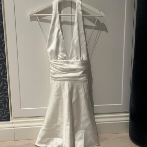 Vit halterneck klänning från Zara - Superfin vit halterneck klänning från Zara i satin🤍Knytband i midjan som inte bara är fina utan också gör det enkelt att ändra hur tajt klänningen ska sitta. Väldigt diskret och smidig dragkedja på sidan🎀 Säljer för att den inte riktigt passar mig över bysten. Endast provad och lappen kvar😇 Storlek XS🌸