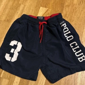 Svarta shorts från Vinson Polo Club - Snygga svarta shorts från Vinson Polo Club med röd snörning och vit text. Perfekta för en avslappnad stil med elastisk midja och nummerdetalj på sidan.