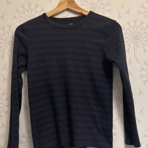 Mörkblå och svart randig tröja från H&M - Säljer en stilren mörkblå och svart randig tröja från H&M. Tröjan har långa ärmar och en rund halsringning, perfekt för kyligare dagar. Passar bra till både jeans och chinos.