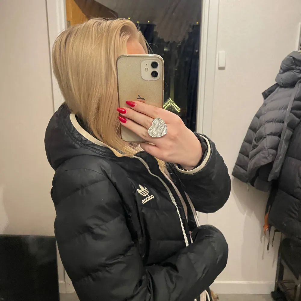 Säljer en svart dunjacka från Adidas med dragkedja och huva. Jackan har en sportig look med det klassiska Adidas-loggan.. Takit.