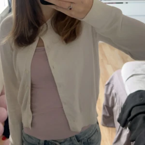 Vit kofta - Säljer en stilren vit kofta med knappar framtill. Perfekt för lager-på-lager och passar till många olika outfits. Koftan har långa ärmar och en mjuk känsla.