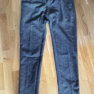 Grå kostymbyxor från Riley - Snygga grå kostymbyxor från Riley i en klassisk stil. Byxorna har en elegant passform och är perfekta för formella tillfällen. De är tillverkade i ett mjukt och bekvämt material med en stilren design.