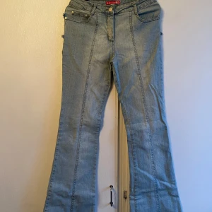 Blå jeans från Blue Collection - Snygga blå jeans från Blue Collection med unika detaljer som dubbla fickor och dekorativa spännen. Byxorna har en bootcut-stil och är tillverkade i en bomullsblandning med lite stretch för extra komfort. (29=36)