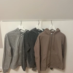 Hoodie med dragkedja - Säljer tre bekväma hoodies i olika färger: ljusgrå, mörkgrå och beige. Alla har dragkedja och huva, perfekta för en avslappnad stil. Passar bra till både jeans och mjukisbyxor, 70kr/st