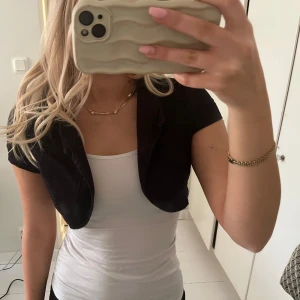 Svart bolerotopp - Snygg svart bolerotopp med korta ärmar. Perfekt för att lägga till en stilren touch till din outfit. Passar bra över linnen eller klänningar.