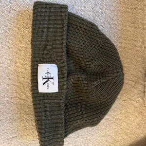Grön ribbad mössa från Calvin Klein - Snygg grön ribbad mössa från Calvin Klein med uppvikt kant och logotyp framtill. Perfekt för kyliga dagar och en stilren look.