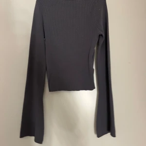 Grå ribbad topp - Säljer en stilren grå ribbad topp med lång ärm och rundad hals. Perfekt för lager-på-lager eller som den är. Enkel och mångsidig design som passar till det mesta.