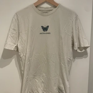Vit t-shirt med fjäril från Jack & Jones - Snygg vit t-shirt från Jack & Jones med en cool fjäril och logga på bröstet. Perfekt för en avslappnad stil. Tillverkad i mjukt material för extra komfort.