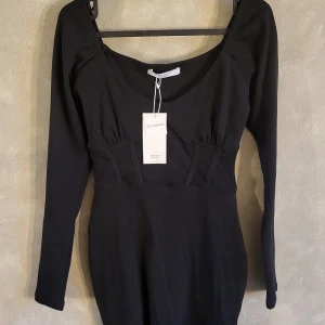 Svart klänning från House Brand - Elegant svart klänning från House Brand med långärmad design och en smickrande passform. Klänningen har en rundad hals och är tillverkad i ett mjukt material som ger en bekväm känsla. Perfekt för en stilren look.