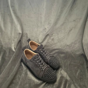Christian Louboutin - Snygga grå sneakers i storlek 43 från Christian Louboutin med nitar på tån och den ikoniska röda sulan. Skorna har snörning och en stilren design som sticker ut. Pris går att diskutera, skriv om du har några funderingar 